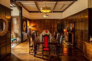 A formal dining room with a long table set for a meal, wooden paneling on the walls, and a chandelier.