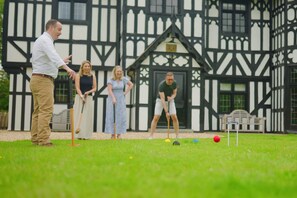 A group of people playing croquet in front of a Tudor-style building.
