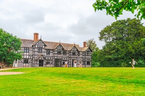 A large, historic building with multiple gables and chimneys, surrounded by a well-maintained lawn and trees.