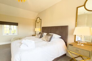 A bedroom with a large bed, a bedside table, a mirror, and a window with a view.