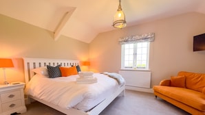 Quarto com cama, luminárias de cabeceira, janela e um sofá laranja.