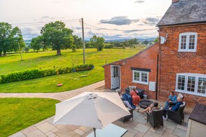 A patio area with outdoor furniture, a large umbrella, and a brick house with a door and windows.