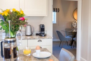 A modern kitchen with a coffee maker, kettle, and a dining area with a table and chairs.