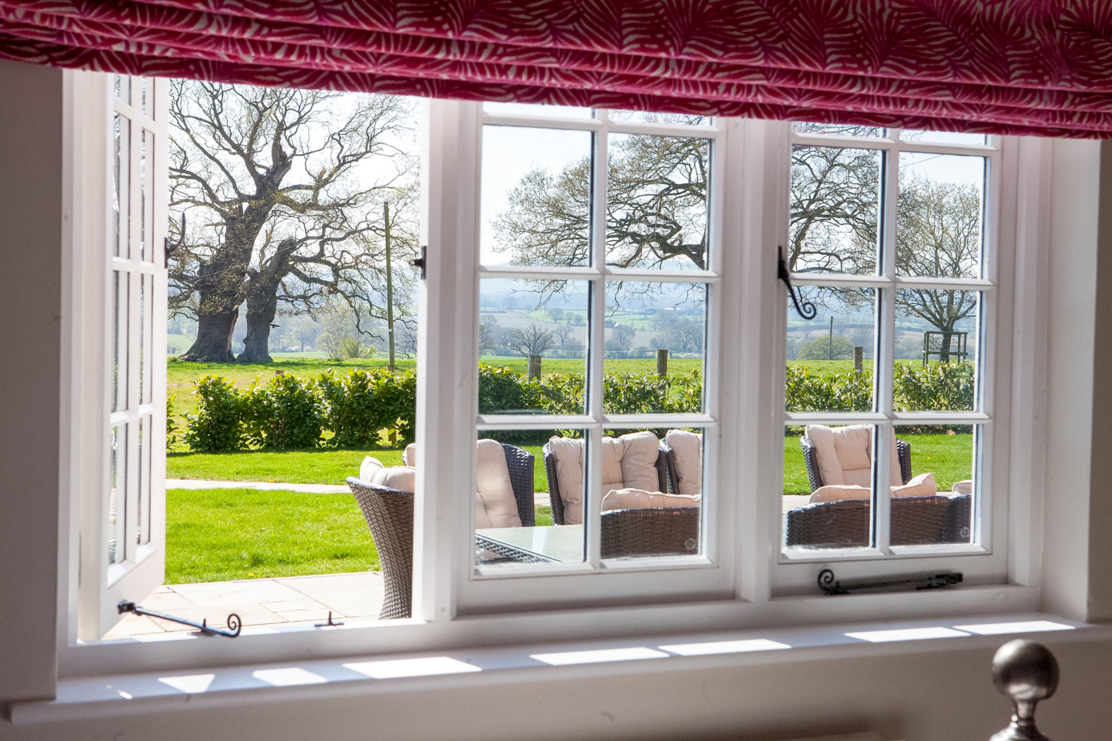 A room with a large window overlooking a garden with chairs and a table.