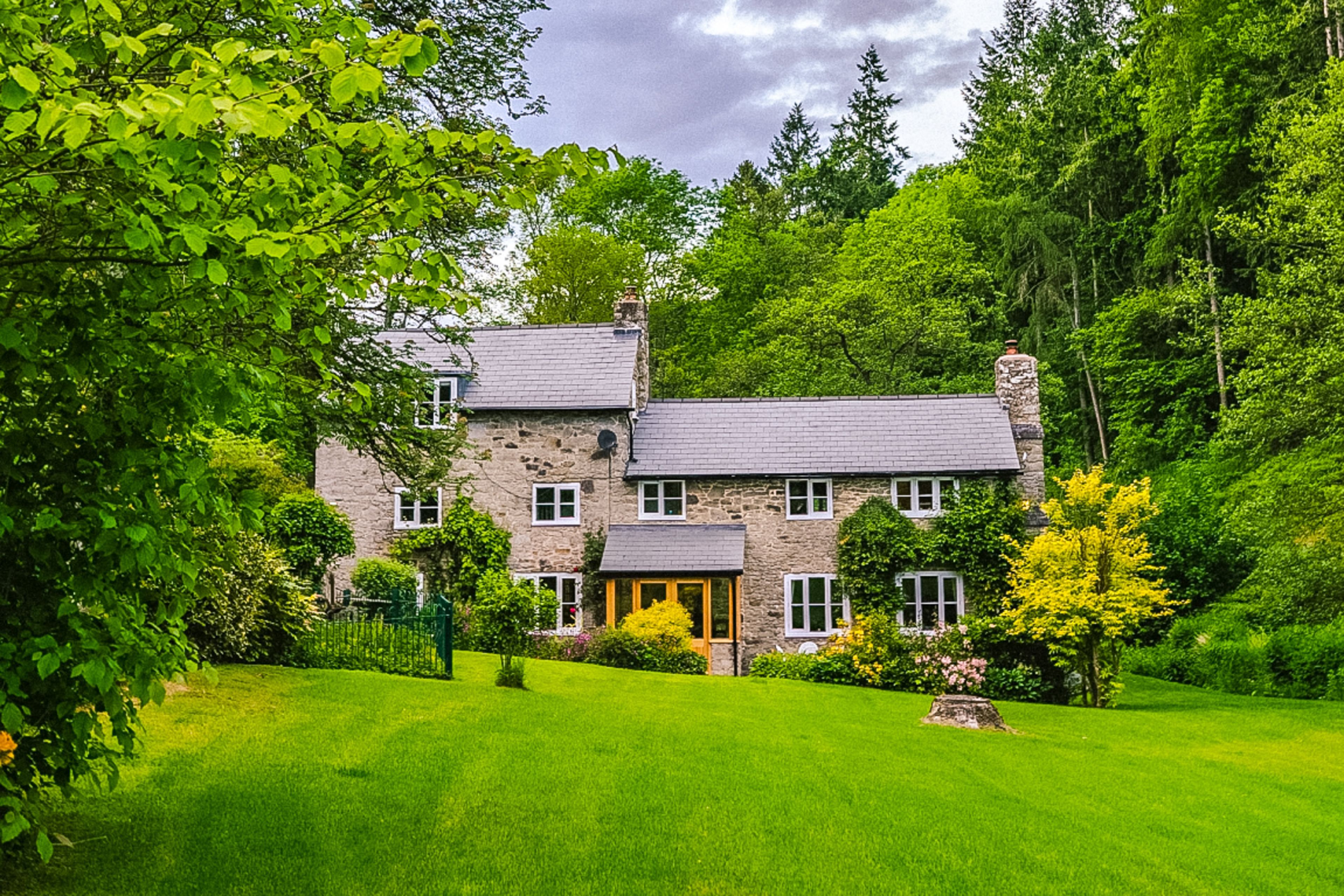 A stone house with a well-maintained lawn and a variety of trees and shrubs.