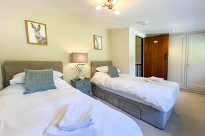 A hotel room with two beds, a bedside table with a lamp, and a wardrobe.