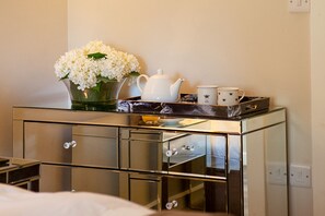 A mirrored cabinet with a white teapot, a tray with a mug, and a vase of white flowers.