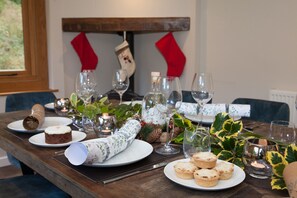 A dining table set with plates, glasses, and candles, with a Christmas stocking and decorations in the background.