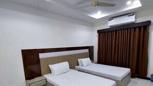 Une chambre d’hôtel avec deux lits simples, une tête de lit en bois, une table de chevet, un ventilateur de plafond et un appareil de climatisation.
