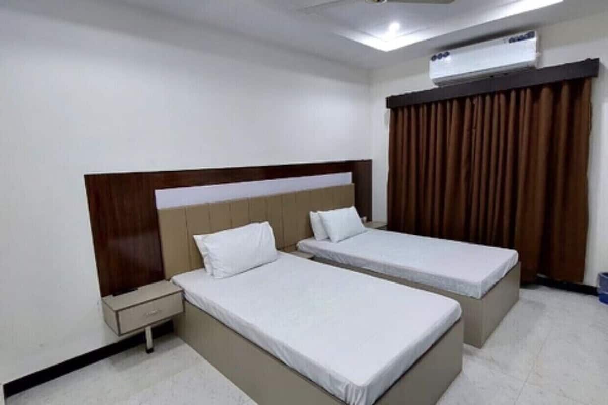 Ein Hotelzimmer mit zwei Einzelbetten, einem hölzernen Kopfteil, einem Nachttisch, einem Deckenventilator und einer Klimaanlage.