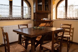 A wooden dining table with six chairs, a cabinet above it, and lace curtains on the windows.