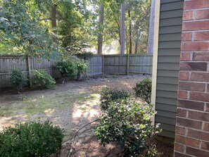 Un jardin avec une clôture en bois, différents arbustes et un tuyau d’arrosage.