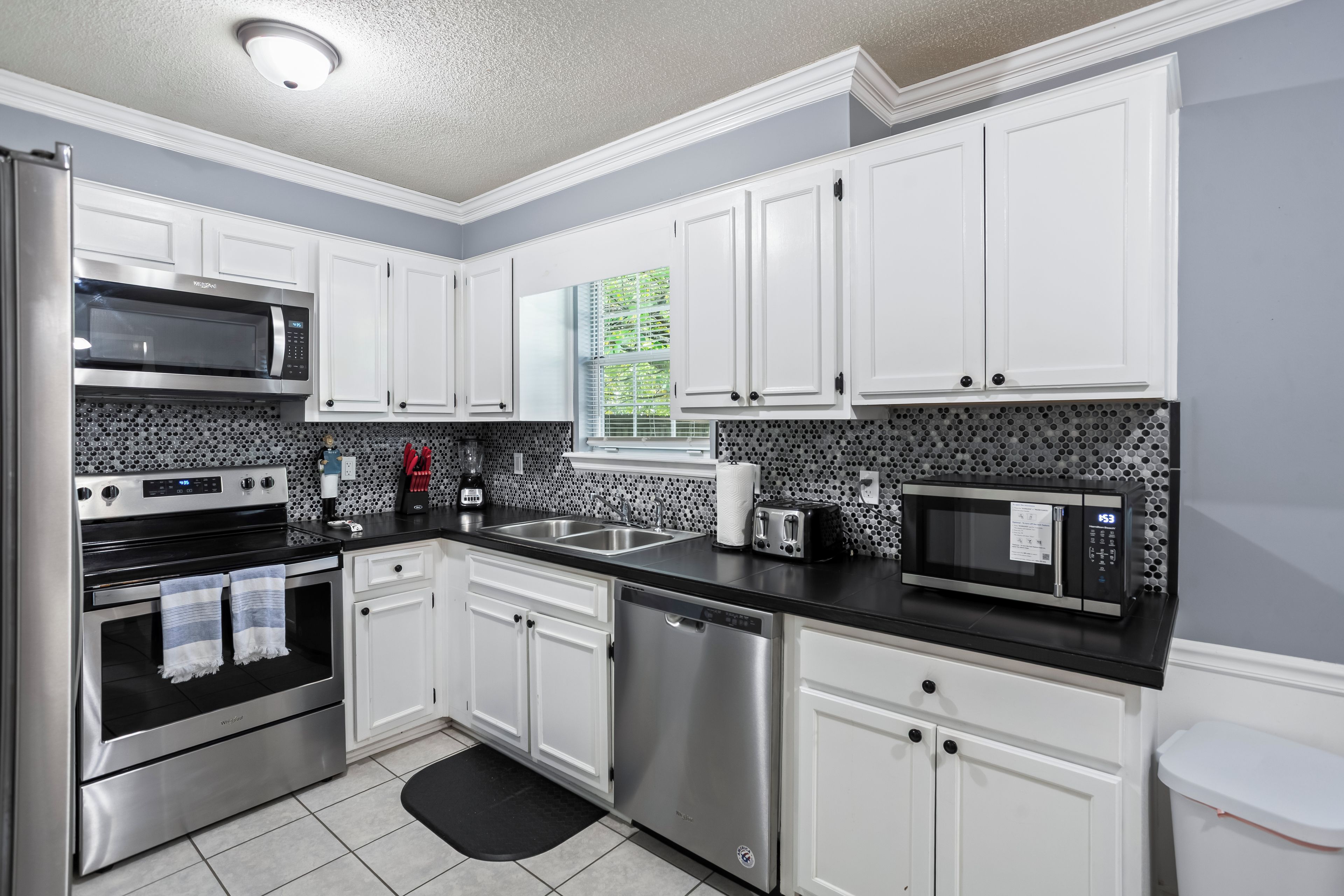 A modern kitchen with stainless steel appliances, white cabinetry, and a black countertop.