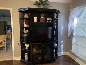 Une bibliothèque d’angle agrémentée de divers objets décoratifs, d’un vase et d’une fenêtre avec des stores.