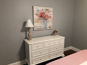 A white dresser with drawers, a lamp, and a floral painting on the wall. - Furnished 3BR Home, Near Bruce’s Field & Polo Grounds, Short & Extended Stays (Aiken)