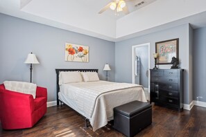 A bedroom with a bed, a red chair, a dresser, and a ceiling fan.