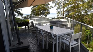 An outdoor deck with a white table and chairs, a sofa, and a potted plant. - Bayview on Bayview, Hyams Beach (Hyams Beach)