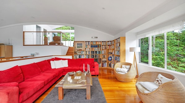 A spacious living room with a red sofa, a coffee table, and a bookshelf filled with books.