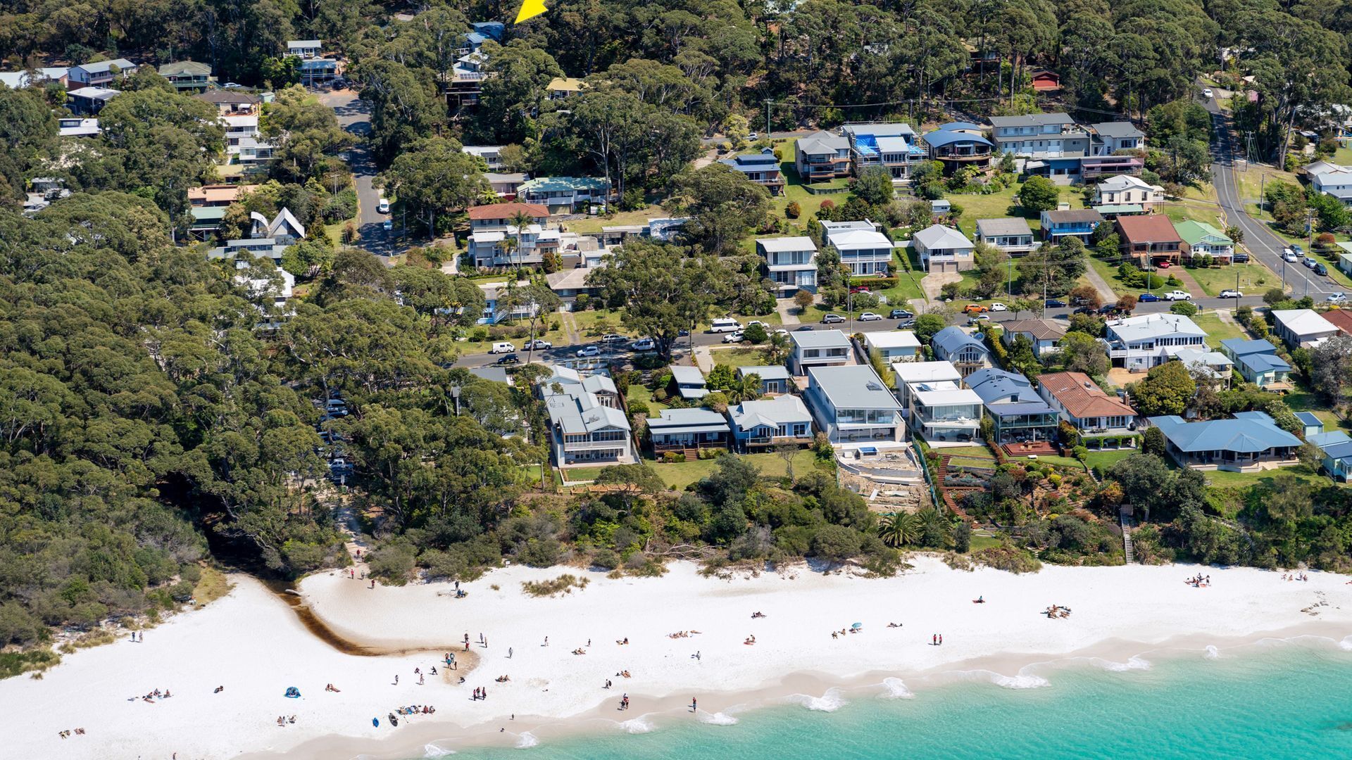 An aerial view of a coastal residential area with houses, a beach, and clear skies.