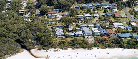 An aerial view of a coastal residential area with houses, a beach, and clear skies.