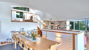 A modern interior with a dining area, a staircase, and a large bookshelf. - Bayview on Bayview, Hyams Beach (Hyams Beach)