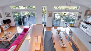 A spacious living area with a large window, a dining table, and a kitchen area with modern appliances. - Bayview on Bayview, Hyams Beach (Hyams Beach)