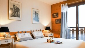 A bedroom with a large bed, two bedside tables with lamps, a wooden headboard, and a balcony with a view.