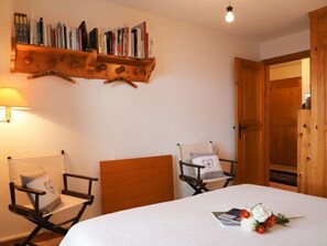 Una habitación con cama, dos sillas, una estantería y una puerta.