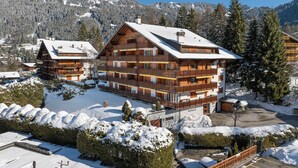 A multi-story wooden building with balconies, surrounded by snow-covered trees and mountains.
