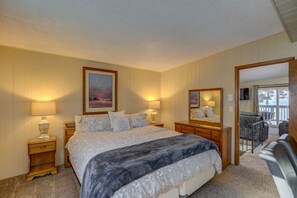 Une chambre avec un grand lit, deux tables de chevet avec des lampes, une commode, un miroir et une vue sur le balcon extérieur.