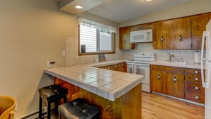 A kitchen with wooden cabinets, a white countertop, a microwave, a stove, and two bar stools. - Annie's Place-Lakefront-Shared dock w/Almost Heaven-Rent both for a 6-room getaway for large groups! (McCall)