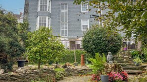 A residential building with a stone pathway, various plants, and a statue in the garden.