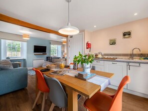 Een gezellige woonkamer met een houten eettafel, oranje fauteuils en een aan de muur bevestigde televisie.
