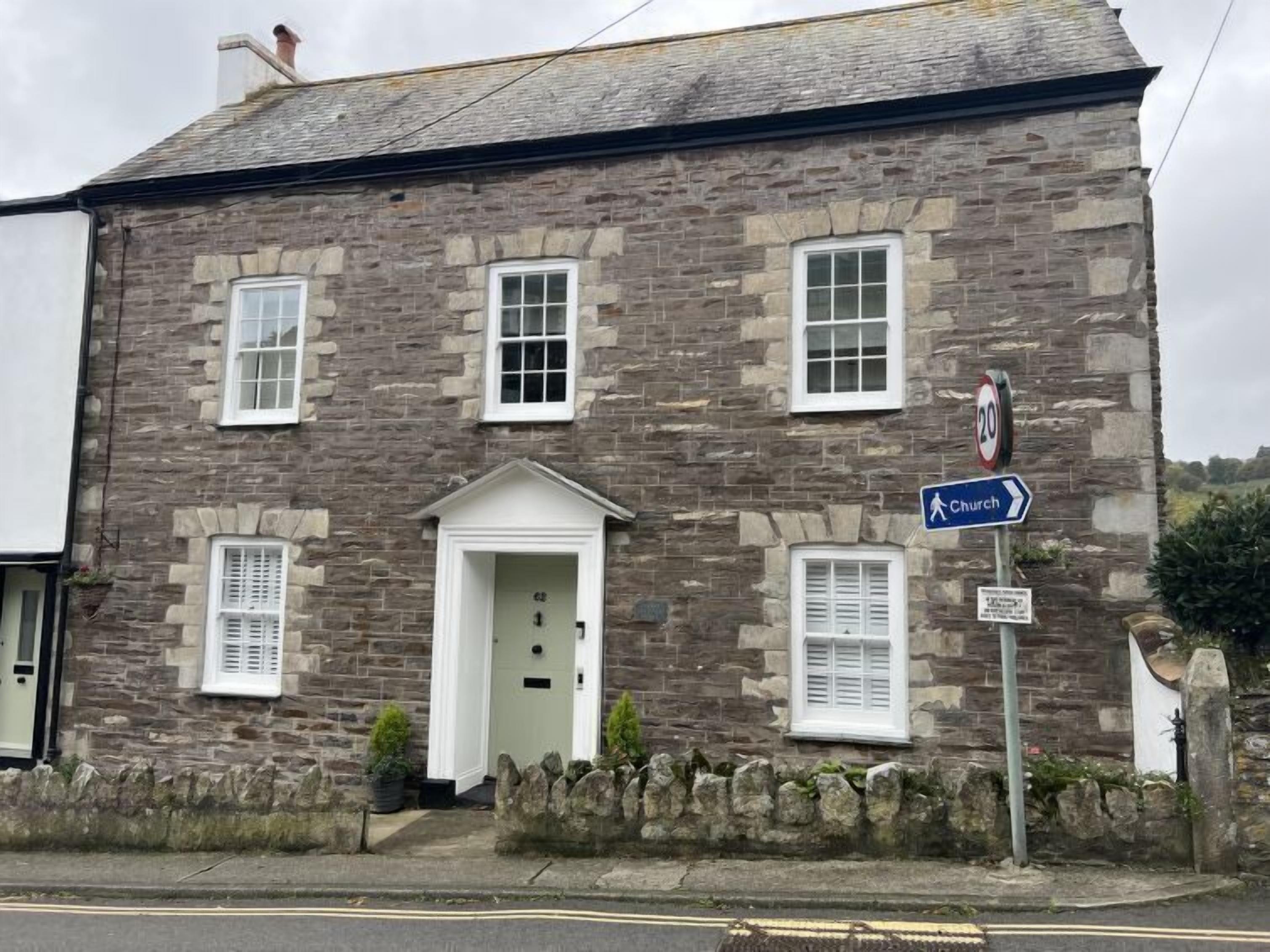 A stone building with a white door and windows, a 'No Parking' sign, and a directional sign for 'Church'.