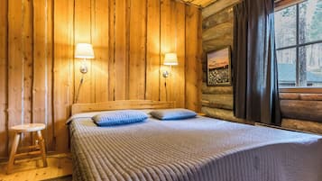 Een houten kamer met een bed, twee wandlampen, een raam met gordijnen en een ingelijste foto aan de muur.