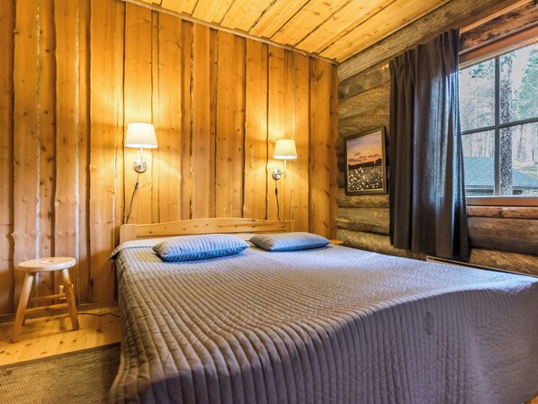 A wooden cabin room with a bed, two wall-mounted lamps, a window with curtains, and a framed picture on the wall. - Kultatunturi by Interhome (Pelkosenniemi)