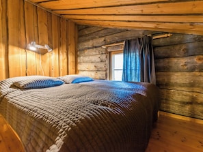 A log cabin bedroom with a bed, a desk lamp, and a window with curtains.