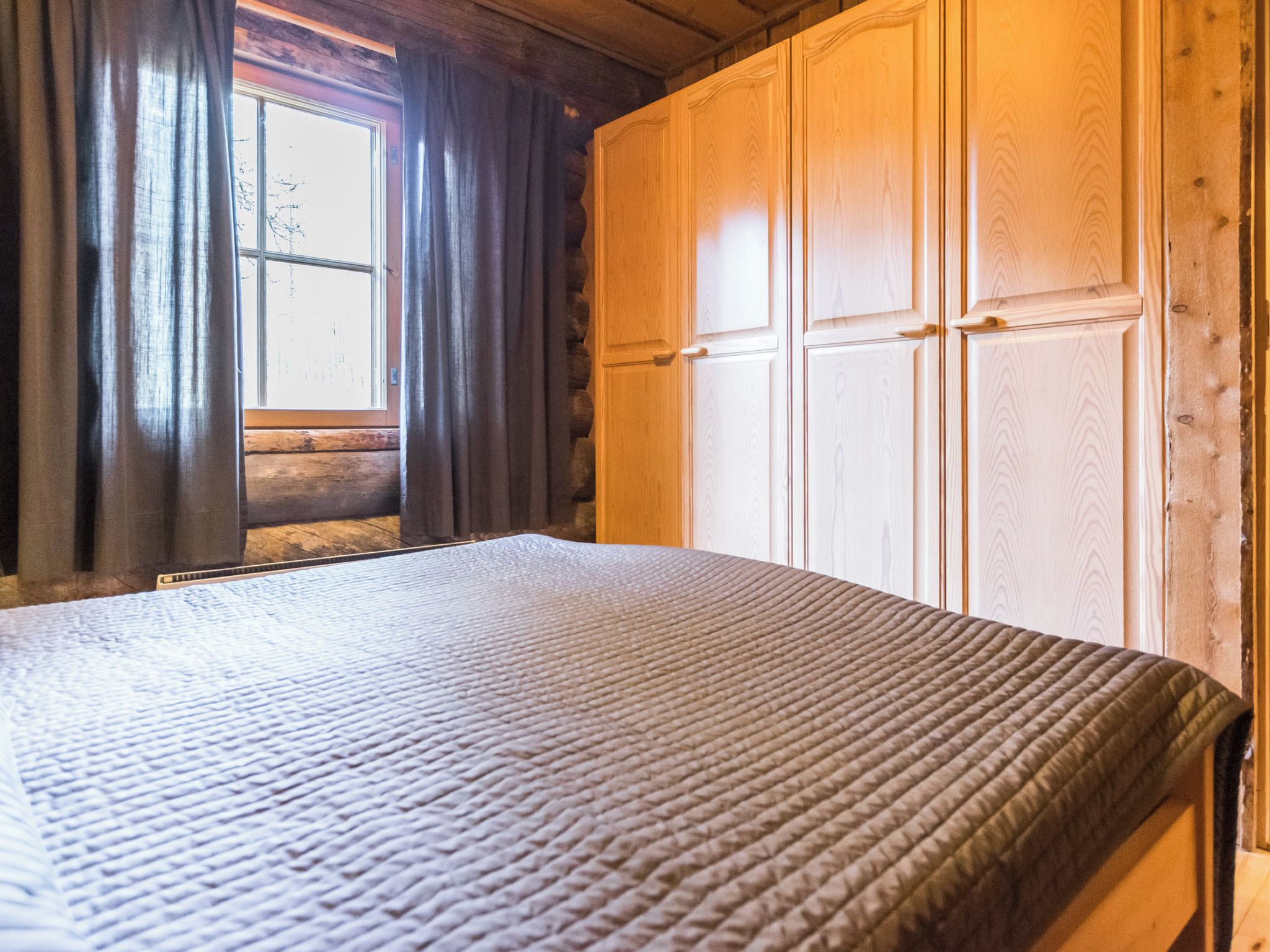 Una habitación con cama, paredes de madera y ventana con cortinas.