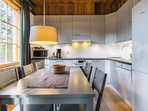 A modern kitchen with a dining table, chairs, a hanging lamp, and built-in appliances.