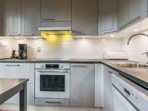 Una cocina moderna con armarios grises, horno empotrado, cafetera y pileta de acero inoxidable.