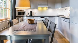 Ett modernt kök med grå skåp, ett matbord med stolar, en hängande lampa och en mikrovågsugn.