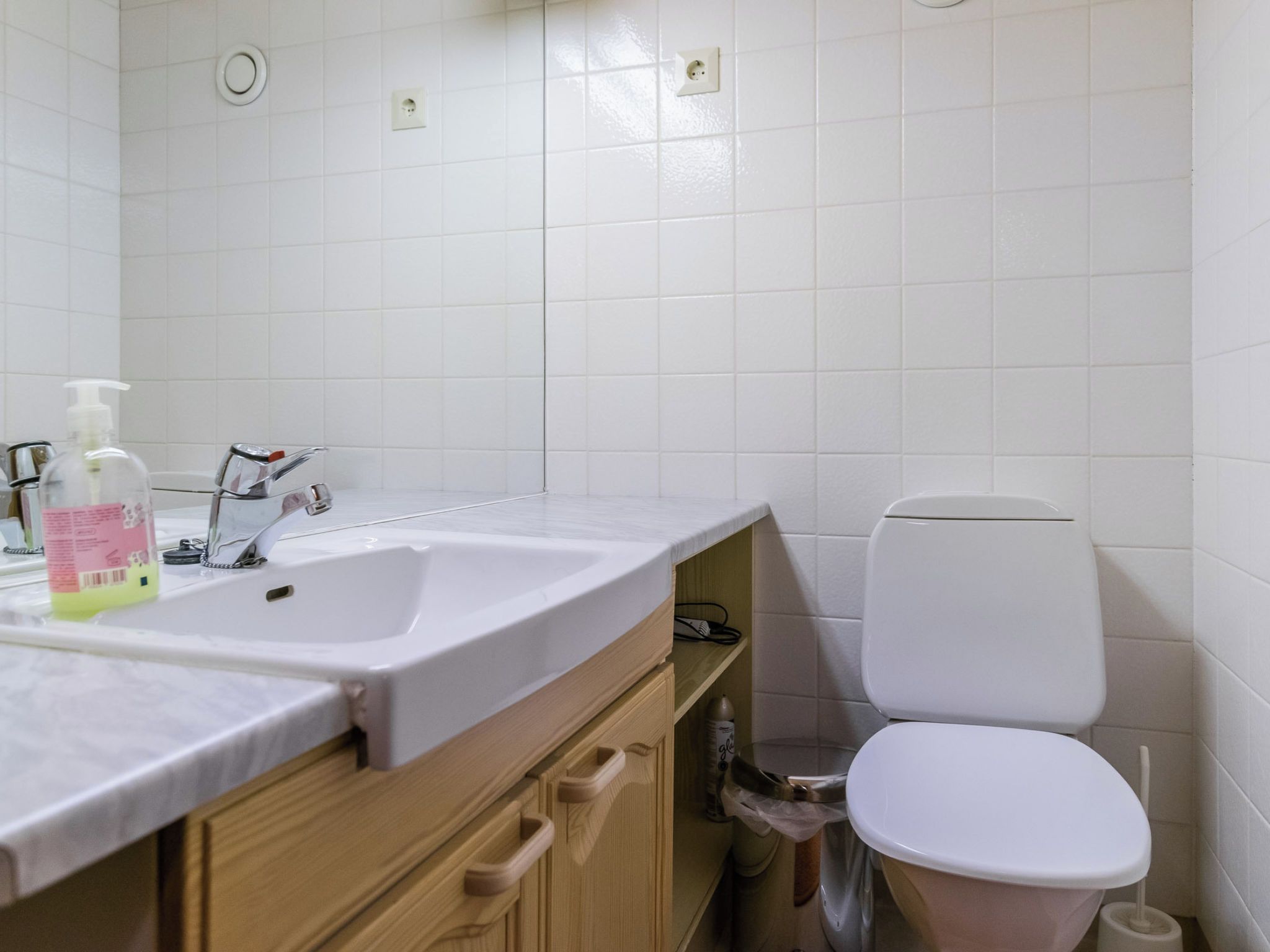 A bathroom with a white sink, a mirror, a toilet, and a wooden cabinet.