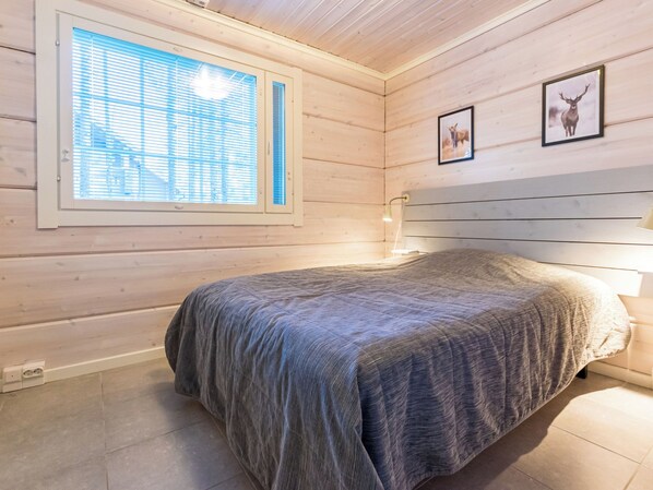 Un dormitorio con cama, ventana con persianas y dos cuadros en la pared.