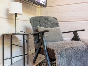 Un fauteuil recouvert d’un plaid en fourrure, une lampe et un téléviseur fixé au mur.