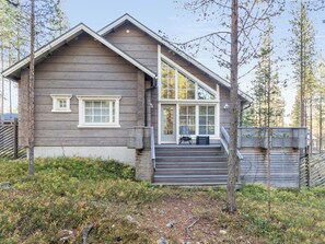 Une cabane en rondins moderne, dotée d’une grande baie vitrée, d’une terrasse en bois et d’un escalier menant à l’entrée.