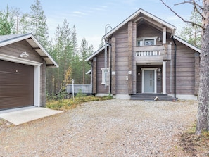 Une maison en bois à deux étages, avec un garage, un porche à l’avant et une allée gravillonnée.