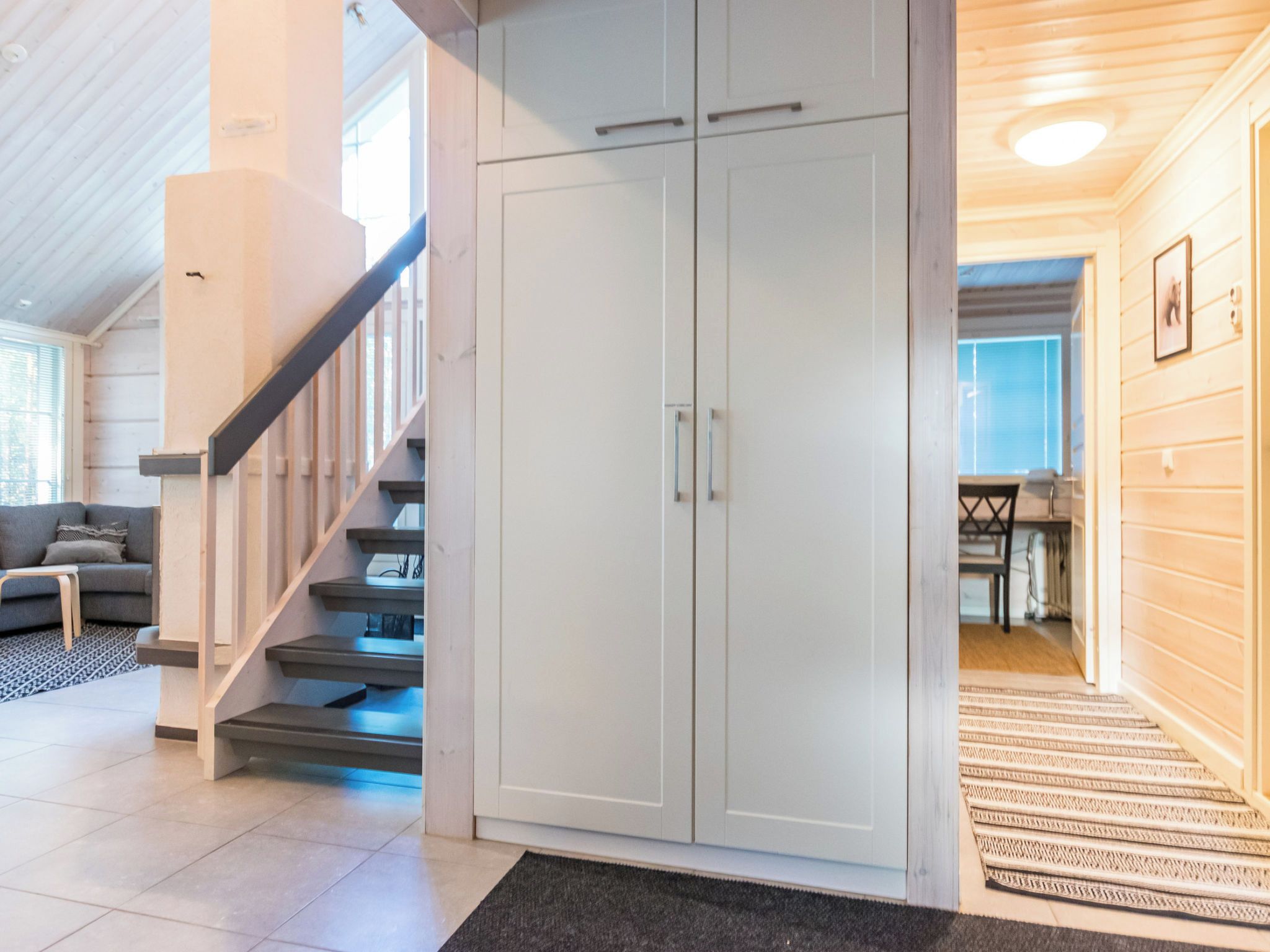 Een trap leidt naar een witte inloopkast, een grijze bank en een kamerbreed tapijt in een goed verlichte kamer met een houten plafond.