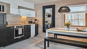 Una cocina moderna con techo de madera, un ventanal con vistas a árboles y una zona de comedor con banco y un jarrón de flores.