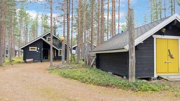 Metsä, jossa on mökkejä, sorapolku ja keltainen ovi.