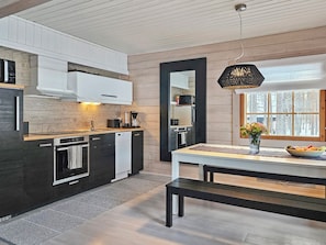 A modern kitchen with a central island, a dining area with a bench, and a large window with a view of trees.